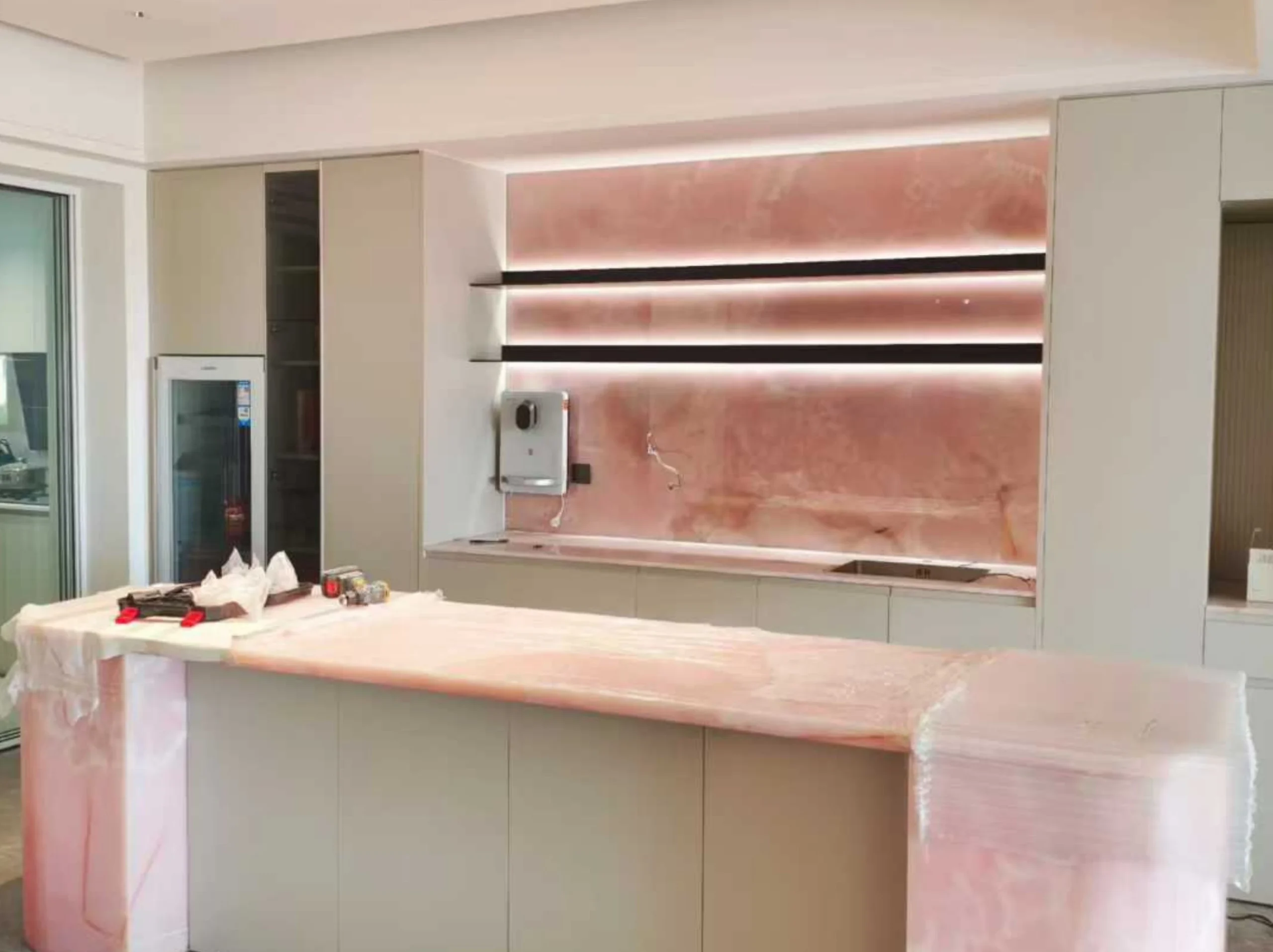 onice-rosso-backlit-kitchen-backsplash-island-03.webp Backlit Onice Rosso kitchen backsplash and custom island with translucent rose-pink stone panels