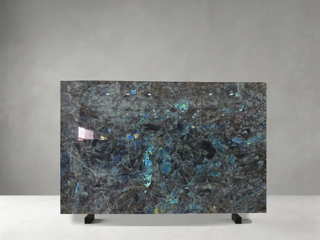 Lemurian Blue Labradorite Granite full slab showing dark blue-green, charcoal, silver and iridescent blue tones with coarse crystalline fields with vivid labradorescent flashes and layered mineral depth